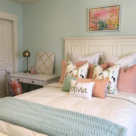 A White Bed Topped With Lots Of Pillows Next To A Dresser And Desk In A
