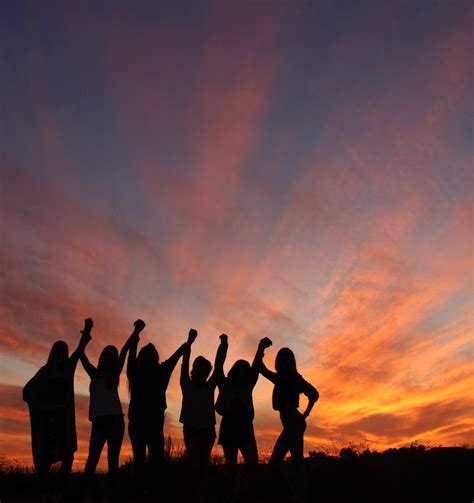 A Group Of People Standing Next To Each Other At Sunset