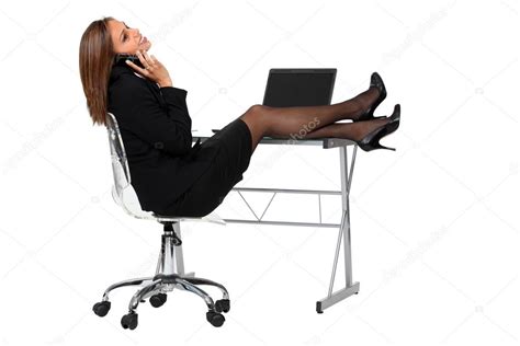 empleada sexy vestida con traje negro sonriendo en el teléfono y estirando sus piernas en su