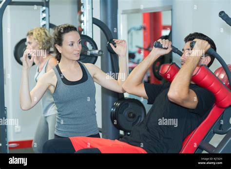 Young Female Coach Assisting Man Using Fly Machine In Gym Stock Photo