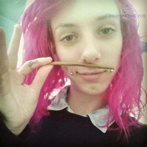 A Girl With Pink Hair And Piercings Holding Up A Stick To Her Face