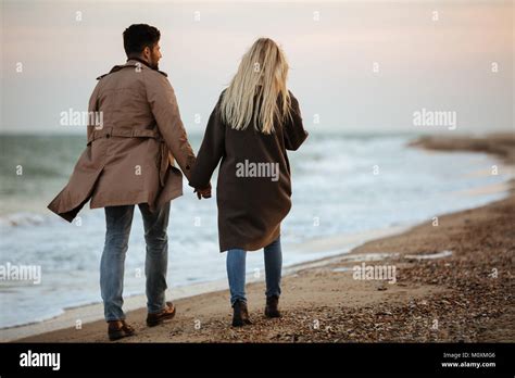 Back View Of A Lovely Couple Holding Hands While Walking Along The