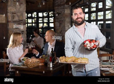 Positive Male Waiter Welcoming Guests To Country Restaurant Stock Photo