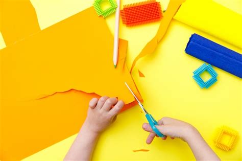 Niño Cortando Papel Naranja De Color Con Unas Tijeras En Una Mesa Para