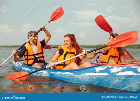 Happy Friends Kayaking On River With Sunset On The Background Stock