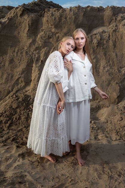 Две привлекательные молодые сестры близнецы позируют на песчаном карьере в элегантной белой