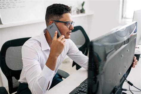 Software Developer Talking Over Mobile Phone Sitting At His Office Desk