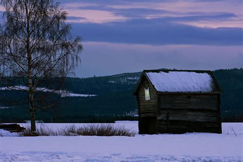 Light Glows In The Window Of A Snall Wooden Cabin In A Snowy Val