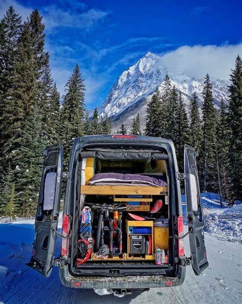 The Back End Of A Van With Its Doors Open On A Snowy Road In Front Of A
