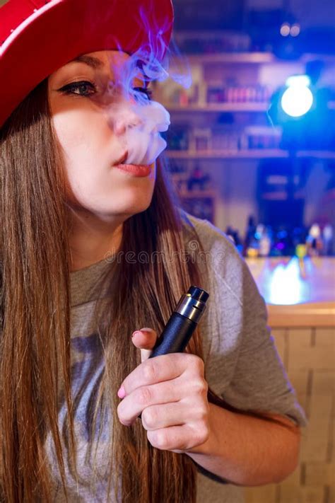 Young Pretty Woman In Red Cap Smoke An Electronic Cigarette At The Vape Shop Stock Image Image