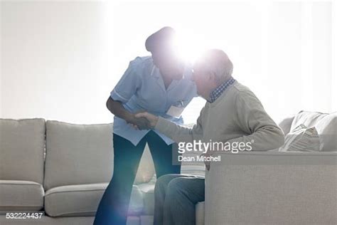 Female Caregiver Helping Senior Man Get Up From Sofa High Res Stock