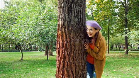 Excited Woman Looking At Camera While Hiding Behind Tree Trunk In Park Stock Image Image Of