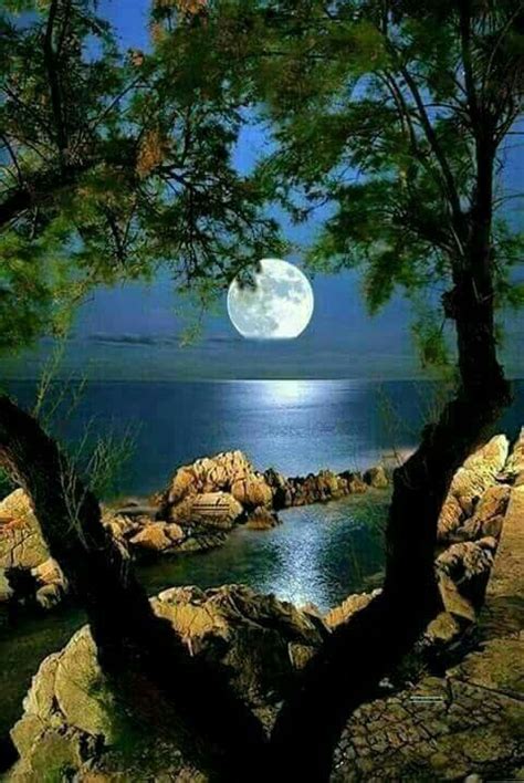 The Full Moon Is Shining Over The Water And Rocks In Front Of It As