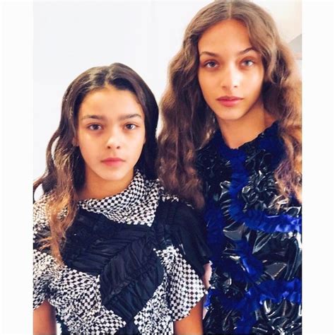 Two Young Women Standing Next To Each Other In Front Of A White Wall