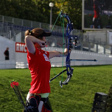 A Woman In Red Shirt Holding Up A Bow And Aiming It At The Target With