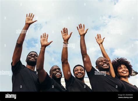 Cheerful Black Men And Woman Raising Hands Against A Blue Sky Stock