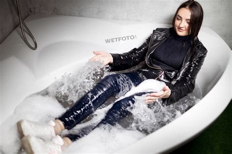 girl takes a bath and gets wet in a winter sweater sneakers socks and leather jacket with jeans