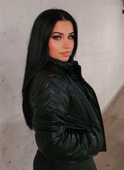 a woman with long black hair wearing a black leather jacket and posing for the camera
