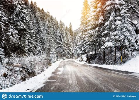 Icy Road Through A Snowy Forest In The Mountains Warmly Lit By A