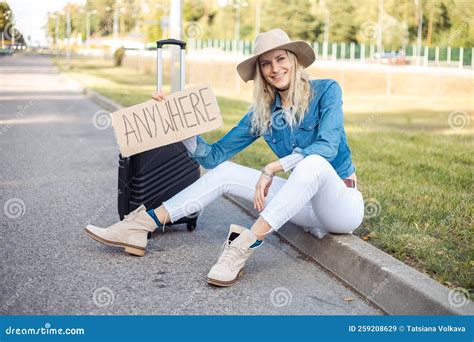 Happy Woman Wait Passing Car Sitting with Suitcase and Cardboard Poster
