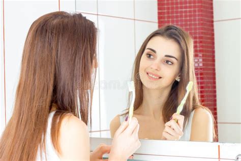 Joyful Young Girl Stands In Front Of A Mirror And Holds In Her Hand The