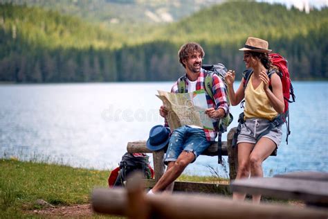 Man And Woman With Backpacks Sitting On Bench Looking At Map Hiking In