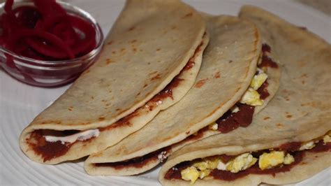 Three Tortillas With Eggs And Sauce On A Plate Next To A Small Bowl Of
