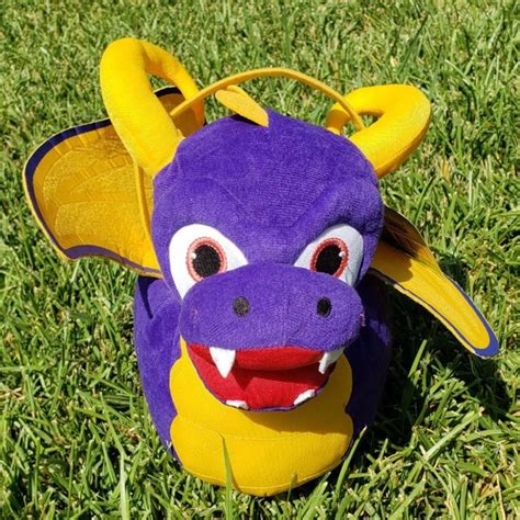 A Purple And Yellow Dragon Stuffed Animal Laying On Top Of Green Grass