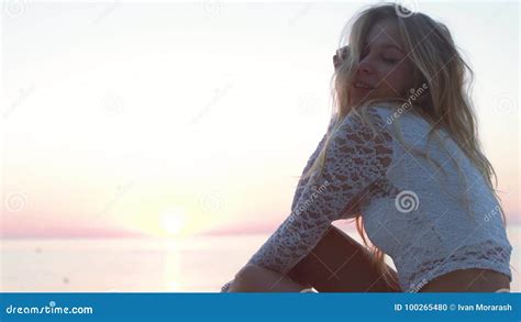Beautiful Blonde Girl On The Beach Looks At The Sea And The Camera Shooted In Golden Hour
