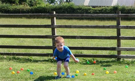 Small Child Playing With Balls And Toys On A Lawn In A Garden On Sunny