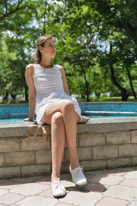 Young Beautiful Girl In Short White Dress Sit Near Fountain Stock Photo