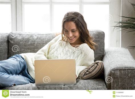 Smiling Woman Enjoying Using Laptop Relaxing At Home On Sofa Stock