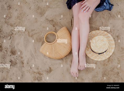 Woman Tanned Legs Straw Hat And Bag On Sand Beach Travel Concept