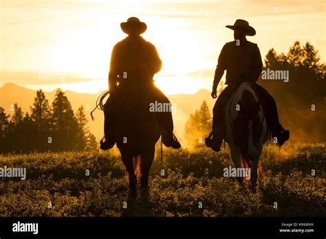 Two Cowboys Riding On Horseback In A Prairie Landscape At Sunset Stock