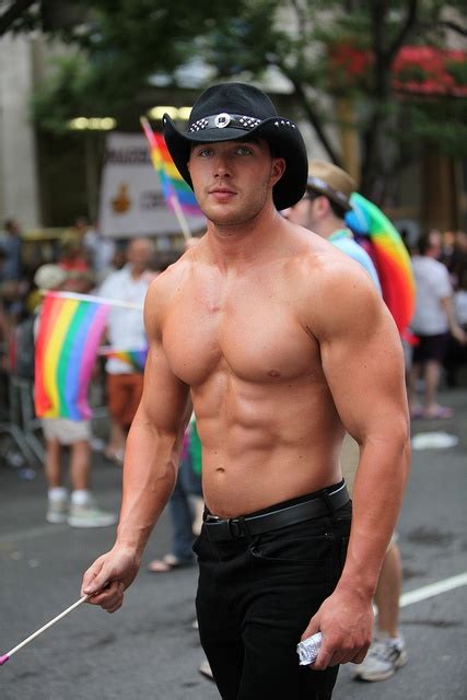 A Shirtless Man Walking Down The Street Wearing A Black Hat And Holding