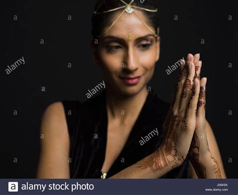 portrait indian woman with bindi and henna tattoos on clasped hands against black background
