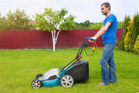 Worker With A Lawn Mower Mows Grass In The Garden Side View Stock