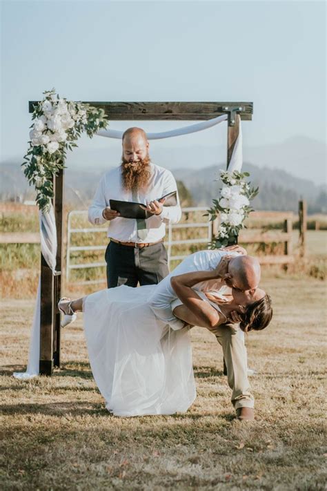Groom Dips Bride For Their First Kiss With Officiant In Background With Wedding Arch First Kiss