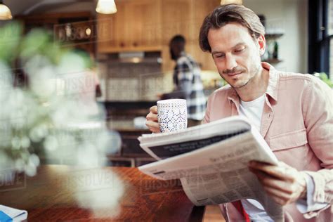 Man Drinking Coffee And Reading Newspaper In Kitchen Stock Photo