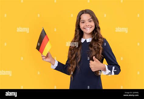 feliz niña adolescente mantener la bandera alemana de fondo amarillo mostrando pulgar hacia