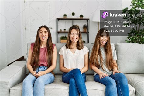 group of three hispanic girls sitting on the sofa at home sticking tongue out happy with funny