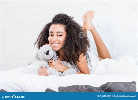Cheerful African American Girl Laying In Bed With Teddy Bear Stock