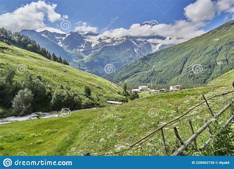 Alpine Green Meadows In The Mountains And Snow Capped Peaks Stock Photo