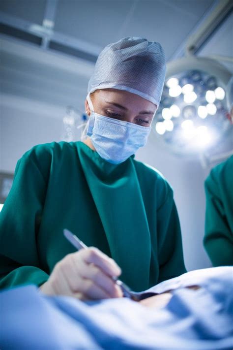 Two Surgeons In Green Scrubs Are Writing On A Piece Of Paper With A Pen