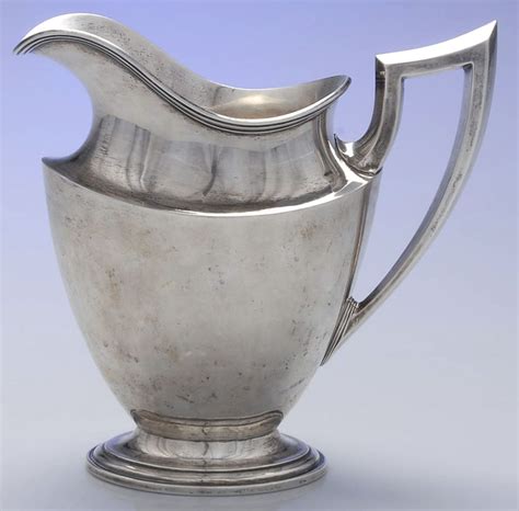 An Antique Silver Pitcher On A White Background