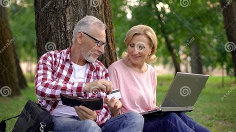 Old Man Giving Credit Card To His Wife Shopping Online On Laptop In