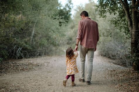 Rear View Of Father And Daughter Holding Hands While Walking On Dirt