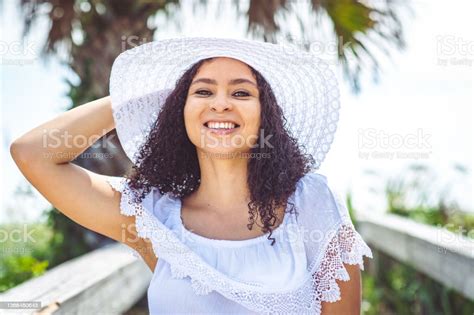Smiling Portrait Of A Afrocaribbean Woman Wearing A Sunhat On A Beach