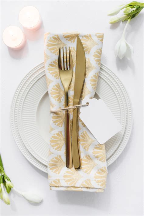 In a formal place setting, the napkin goes neither under the fork or the knife, but on the charger, a small decorative plate placed on top of the dinner plate. Dining table setting with folded napkin and candles on ...