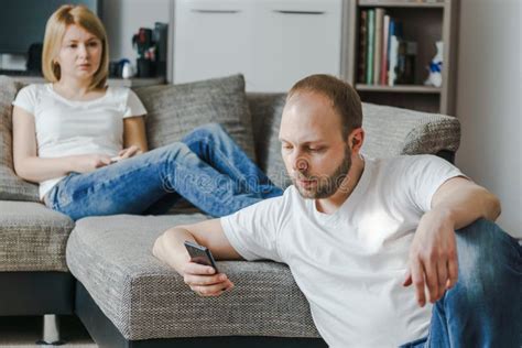Young Woman Sitting Sofa Talking To Her Husband Using His Cellphone Their Living Room Stock